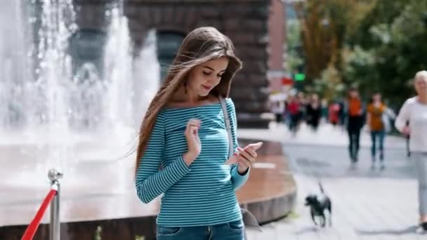 Ung, snygg tjej använder en smartphone på en stadsgata, en kvinna skriver ut ett meddelande, chating — Stockvideo