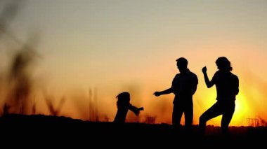 Baba ve kızın siluetleri el ele tutuşuyor ve tarlada yaz gün batımında daireler çiziyor