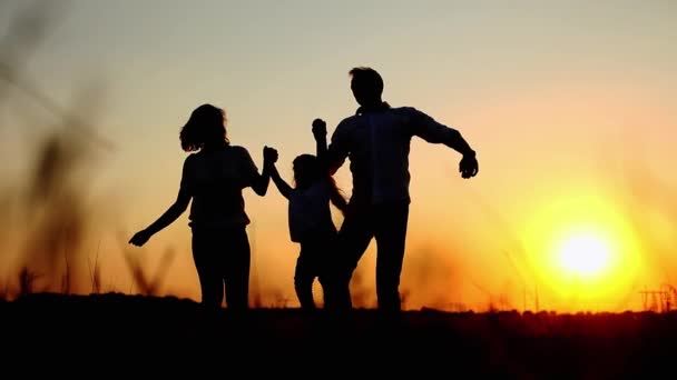 Silhouetten glücklicher Eltern werfen ihre Tochter in die Höhe und umarmen sich bei Sonnenuntergang im Sommer, während sie ihren Urlaub genießen — Stockvideo