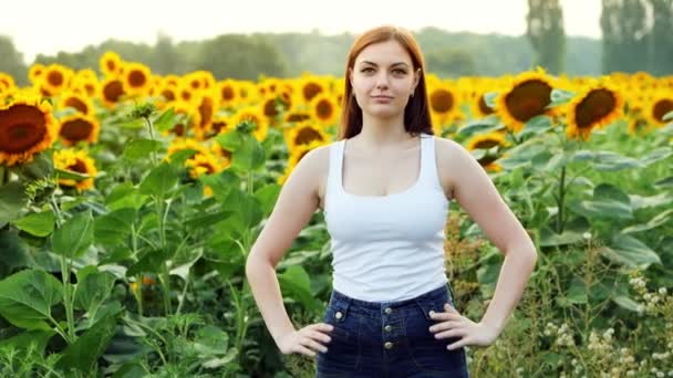 Gyönyörű fiatal nő gazda nézi a kamerát, és mosolyogva a háttérben egy mező napraforgók — Stock videók