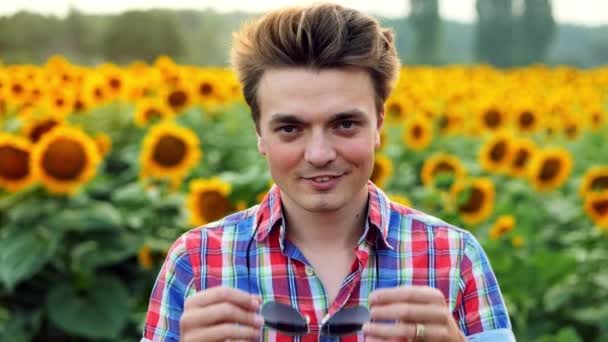 Chladný a stylový moderní mužský farmář si klade brýle na pozadí pole slunečnic — Stock video