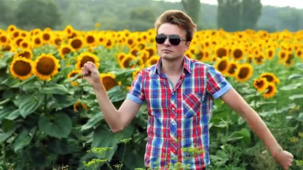 Fresco macho-agricultor bailando divertido en el campo de girasoles, satisfecho y positivo en la puesta del sol. Concepto agrícola — Vídeos de Stock