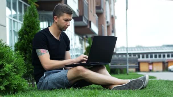 Freelancer work on laptop in the open air while sitting on grass — Stock Video