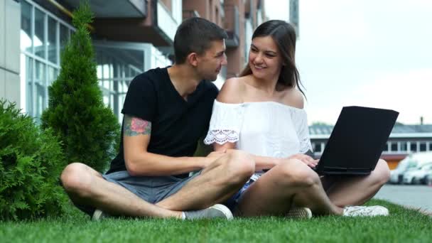 Šťastný pár provádí nákupy online pomocí notebooku, volí zboží, sedí na trávě — Stock video