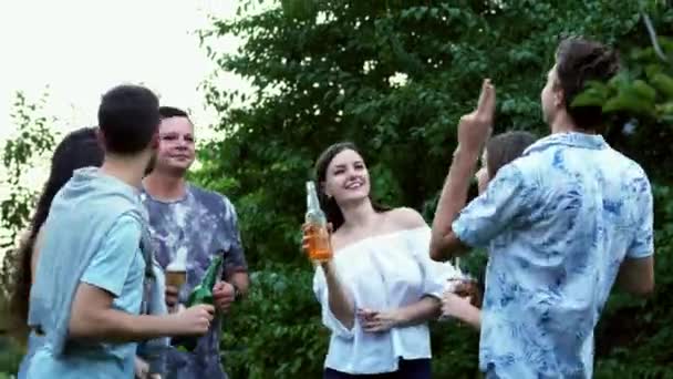 Група друзів клонують пляшки, п'ють пиво, люди танцюють і обіймаються в парку, вечірка . — стокове відео