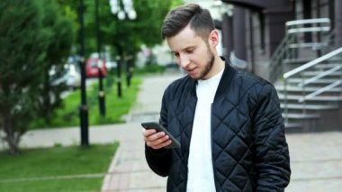 Yakışıklı sakallı adam sokakta telefon kullanır, metin yazarak, sohbet