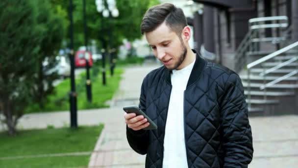 Όμορφος άνθρωπος με γένια χρησιμοποιεί το τηλέφωνο στο δρόμο, πληκτρολογώντας κείμενο, συνομιλία — Αρχείο Βίντεο