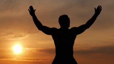 Güçlü bir adamın silueti gün batımında tek başına nefes egzersizi yapar, gün batımında meditasyon yapar.