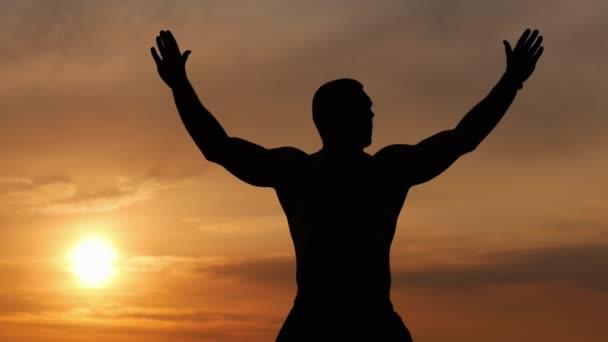 Силует сильного чоловіка робить вправи на самоті під час заходу сонця, роздумуючи на заході сонця — стокове відео