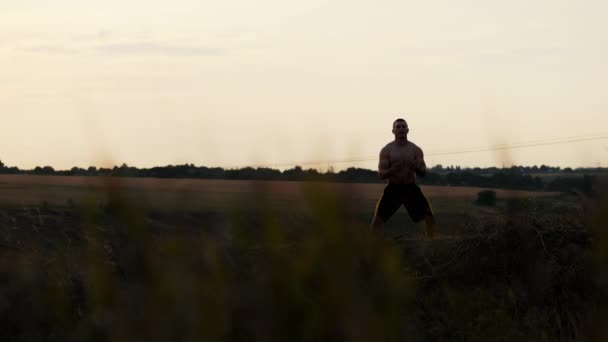 La silueta de un hombre musculoso hace un ejercicio de respiración solo al atardecer, meditando al atardecer — Vídeo de stock