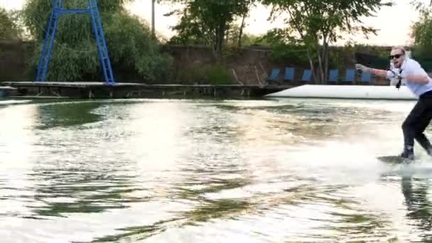 Extremo empresario sorprendido en un traje con una corbata y gafas de sol paseos en wakeboard en un lago — Vídeo de stock