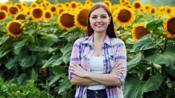 Όμορφη νεαρή γυναίκα αγρότης στο γήπεδο με ηλιοτρόπια κοιτάζοντας την κάμερα και χαμογελαστή — Αρχείο Βίντεο