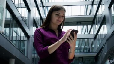 Mutlu iş kadını bir binanın arka planına karşı cep telefonu bakıyor