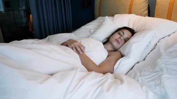 Привлекательная молодая женщина просыпается и растягивается рано утром, лежа в постели — стоковое видео
