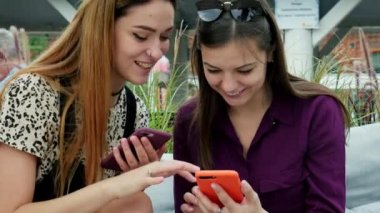 Cep telefonu kullanan ve konuşan iki çekici genç kadın. Terasta iyi vakit geçirmenin keyfini çıkaran arkadaşlar