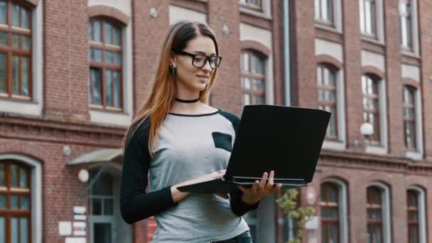 Porträtt av kvinnlig student eller frilansare, kvinna i glasögon stående och arbetar på laptop, flicka på college bakgrund i Campus tittar på kamera — Stockvideo