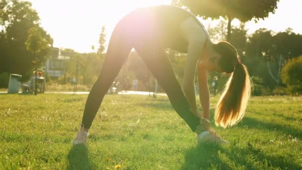 Mujer deportiva haciendo ejercicios de fitness y estiramiento, entrenamiento en el parque al atardecer, concepto de estilo de vida saludable y deportivo — Vídeo de stock