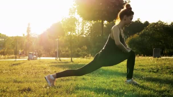 Atletyczna kobieta robi ćwiczenia rozciągające w parku o zachodzie słońca. Fitness, trening aerobowy, zdrowa i sportowa koncepcja stylu życia — Wideo stockowe