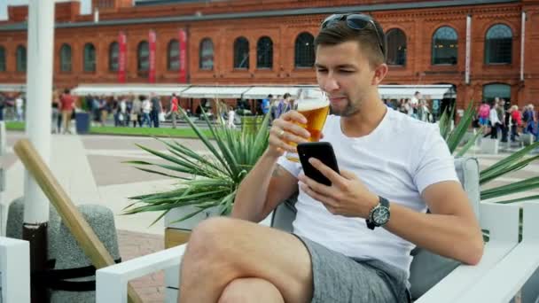 Moderne jonge man gebruiken mobiele telefoon en drankjes een koud biertje. Genieten van een goede tijd op het terras — Stockvideo