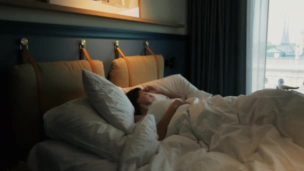 Привлекательная молодая женщина спит в гостиничном номере рано утром, лежа в постели — стоковое видео