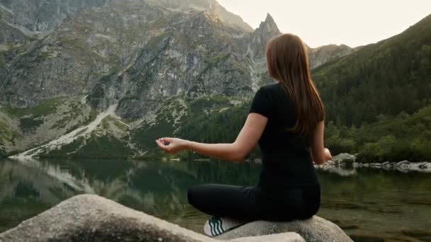 Healthy young woman meditates on a mountain lake, practicing yoga, enjoys the tranquility high in the mountains — Stock Video