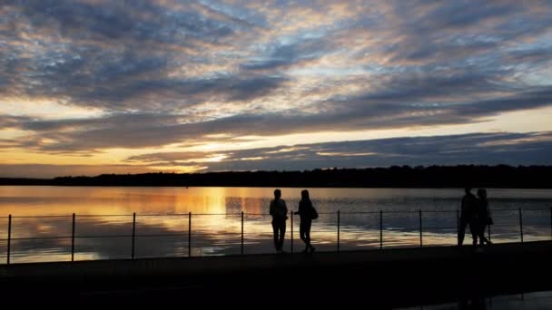 Silhuett av turister, människor går på en bro på sjön under solnedgången på kvällen — Stockvideo