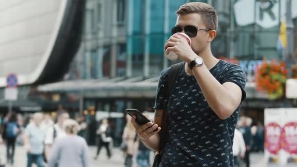 Modern man with a cup of coffee use mobile phone on crowded city street — Stock Video