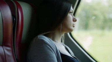 Otobüs yolculuğunda yalnız kadın seyahatportresi, hırsla pencereye bakarak ve müzik dinleme