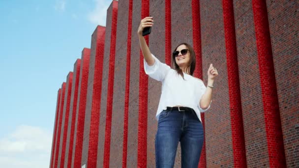 Mooie vrouw toerist maakt gebruik van een mobiele telefoon voor video-oproep aan vrienden in de buurt van een moderne bakstenen gebouw, expositiecentrum — Stockvideo