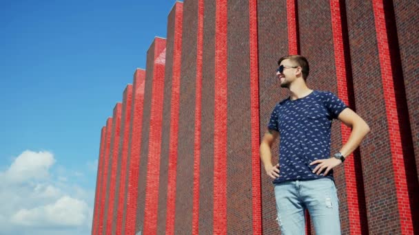 Happy uomo turistico si trova sulla strada della città in occhiali da sole vicino a un moderno edificio in mattoni — Video Stock