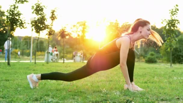 Kaunis urheilullinen tyttö tekee kunto ja venyttely harjoituksia, koulutusta puistossa auringonlaskun aikaan — kuvapankkivideo