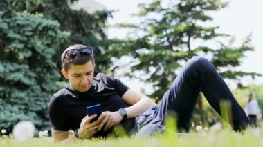 Mutlu adam şehir parkında çim üzerinde dinlenirken cep telefonu kullanıyor, sohbet ediyor.
