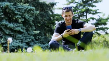 Mutlu adam şehir parkında çim üzerinde dinlenirken cep telefonu kullanıyor, sohbet ediyor.