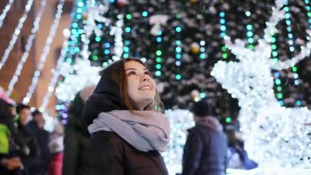 Mulher bonita olha para a neve, cidade da noite decorada para o Natal e Ano Novo — Vídeo de Stock