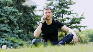 Cep telefonuyla konuşan, parkta çimlerin üzerinde oturan bir adam.