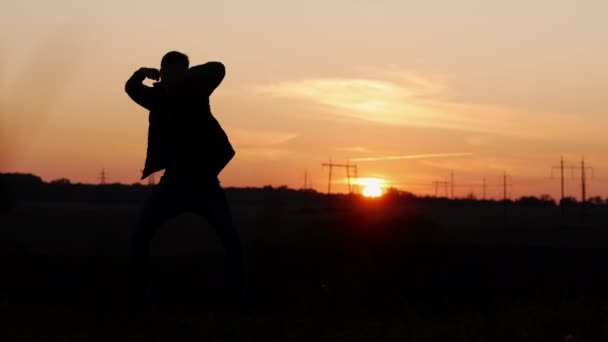 Silhueta de um homem louco dançando em um campo ao pôr do sol — Vídeo de Stock