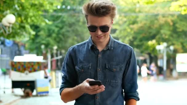 Modern young man uses the phone on the street, typing text — Stock Video