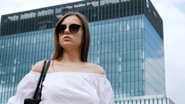 Confident businesswoman standing on a city street, modern business center on background — Stock Video