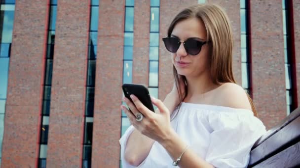 Уверенная женщина пользуется мобильным телефоном на улице, современное кирпичное здание — стоковое видео