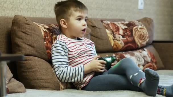 Niño pequeño juega en el videojuego en el sofá en casa en vacaciones — Vídeos de Stock