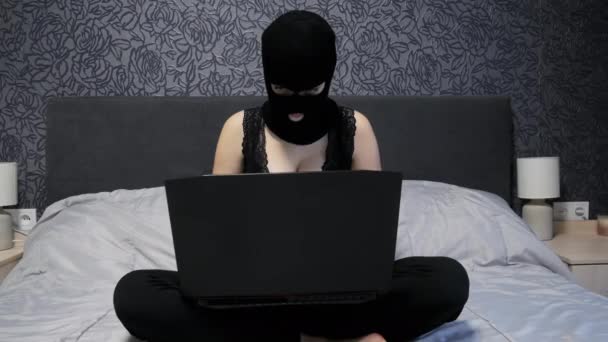 Сексуальна смішна жінка-хакер, одягнена в чорну балаклавську маску і бюстгальтер з розкішними грудьми, що працюють на ноутбуці, хакерська атака — стокове відео