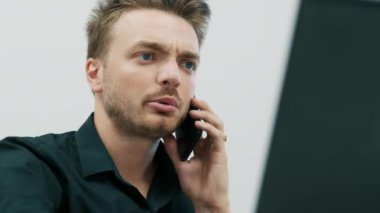 Yakışıklı genç sakallı adam cep telefonuyla konuşuyor ve ofiste laptop kullanıyor..