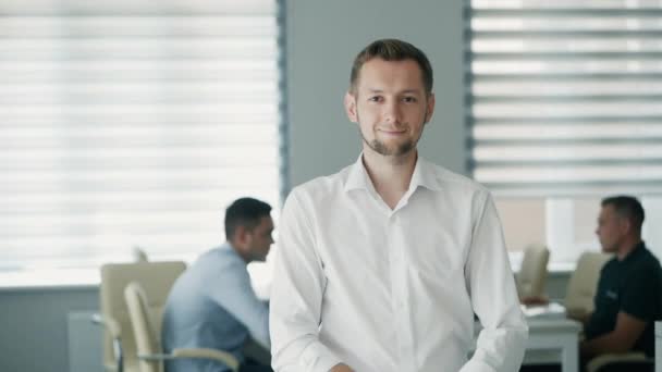 Selbstbewusst fröhlicher Büroangestellter mit Blick in die Kamera im modernen Büro, positiver männlicher Angestellter mit lächelndem Gesicht zufrieden mit guter Berufskarriere — Stockvideo