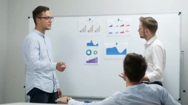 Yöneticiler diyagramları ve grafikleri tartışıyor, ofiste çalışıyorlar.