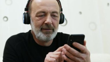 Kablosuz kulaklıklı orta yaşlı bir adamın portresi müzikten hoşlanıyor, cep telefonuyla internette yeni müzikler arıyor