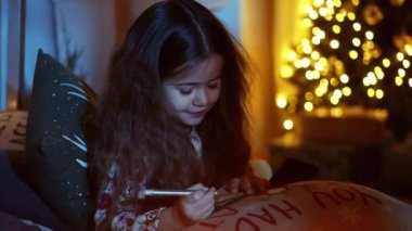 Yatakta uzanmış tatlı küçük kız Noel için dekore edilmiş Noel Baba 'ya mektup yaz, bir dilek tut, Noel ve yeni yıl arifesi.