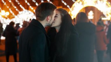 Kalabalık caddede öpüşen mutlu çift, arka plandaki çelenklerle flört, yeni yıl Noel 'i