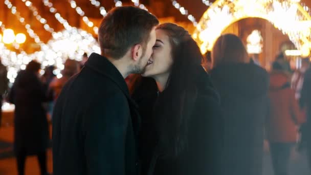 Счастливая пара целуется на переполненной улице, свидание на фоне гирлянд, новогоднее Рождество — стоковое видео