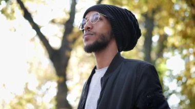 Gözlüklü melez bir adamın sonbahar portresi ve geleneksel bir şapka, etrafa bakıyor, ağır çekimde.