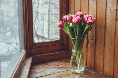 Pencerenin yanında vazoda laleler var. Pencerenin yanında ahşap bir masa üzerinde bir vazo içinde çiçek buketi.